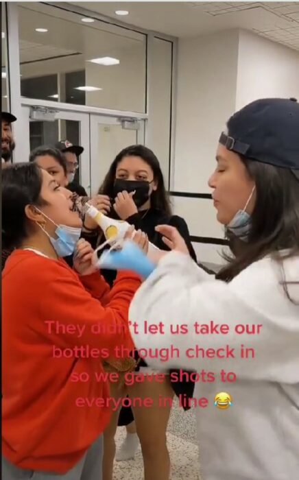 foto de una chica a punto de dar un trago a una botella en un aeropuerto 