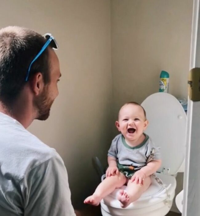 man sitting in front of his baby who is on the toilet