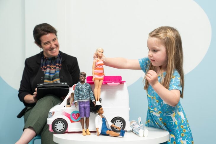 Investigadora obersevando a niña jugar con muñecas Barbie 