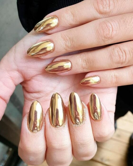 Chica usando unas uñas con tonos dorados brillantes 