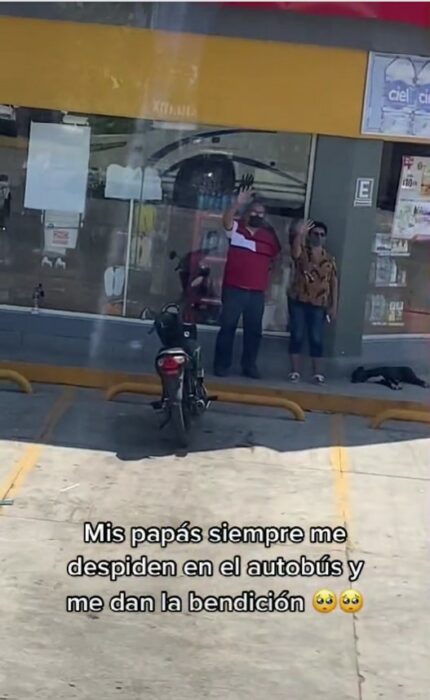 a man and a woman standing in front of an Oxxo waving goodbye 