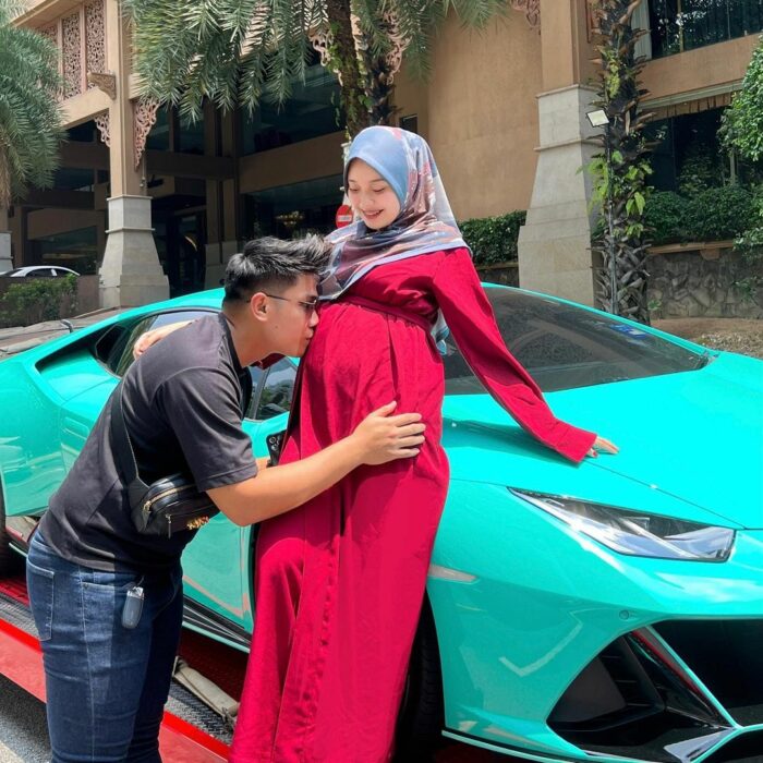 man giving a kiss to the belly of his wife who is on a Lamborghini 