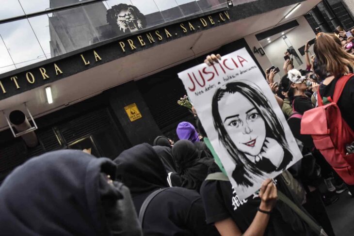 Personas en una marcha frente a un edificio federal con pancartas 