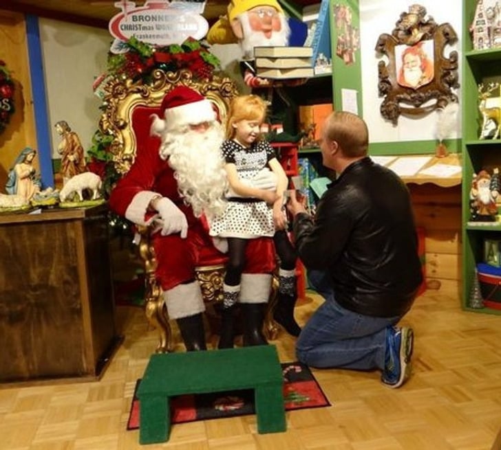 hombre hincado frente a una niña que es cargada por un Santa Claus 