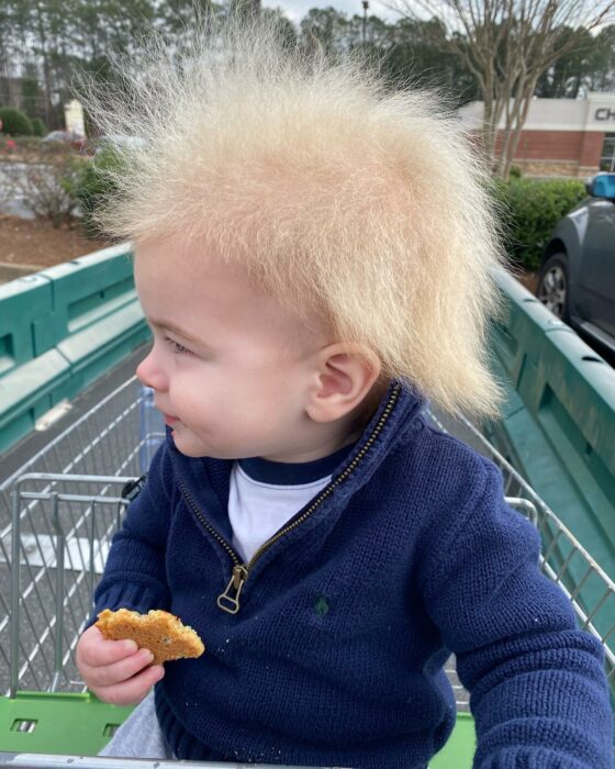 Niño comiendo una galleta sentado en un carro de supermercado 