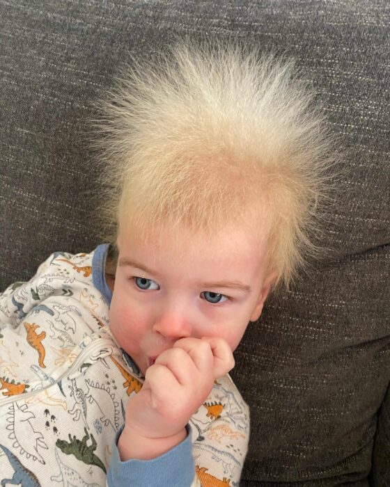 Niño con el cabello alborotado con el dedo en la boca 