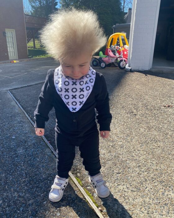 Niño mostrando su cabello rubio alborotado en el patio de una casa 