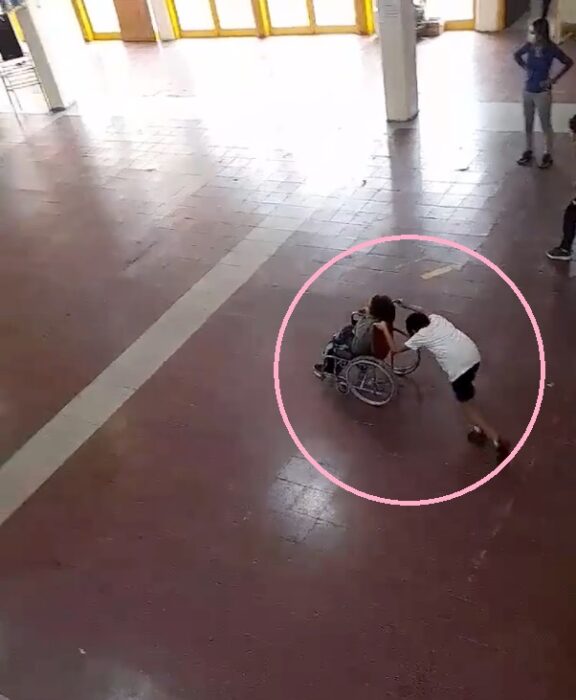 Child pushing a wheelchair;  Little boy helps his classmate in a wheelchair in the middle of class