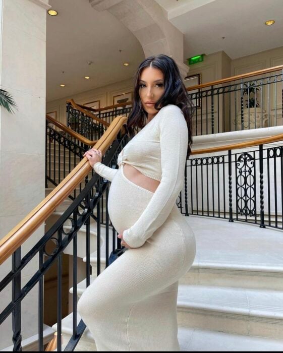 mujer embarazada parada en unas escaleras portando un vestido en color blanco 