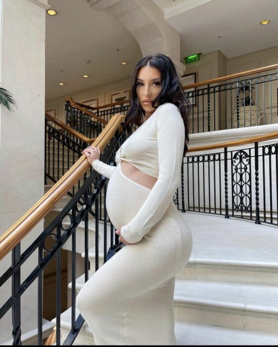 pregnant woman standing on some stairs wearing a white dress 