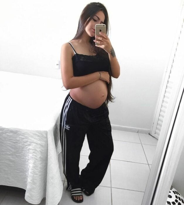 chica embarazada mostrando su pancita y tomándose una foto frente al espejo en su recámara