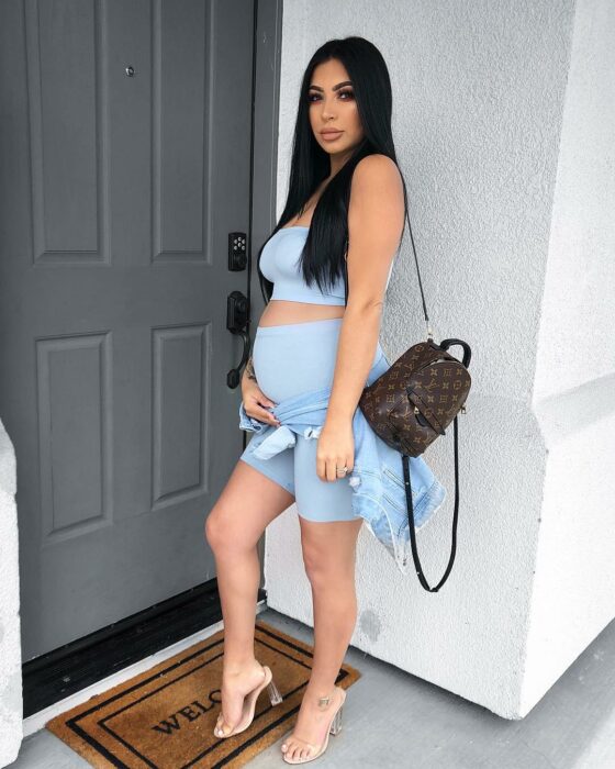 Photograph of a pregnant girl standing in front of the door of a house 