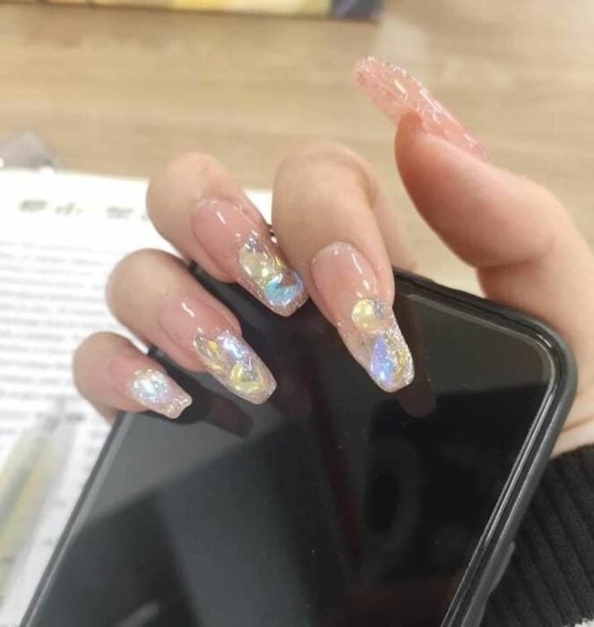mano de una chica mostrando sus uñas mientras sostiene su celular 