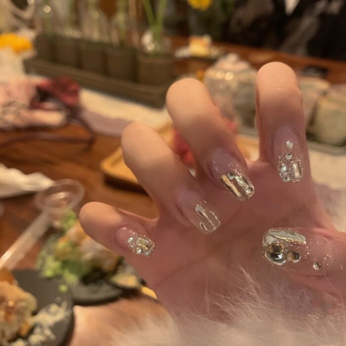 mano de una chica usando uñas acrílicas con estilo francés pero dorado con algunos toques de gotas de agua 