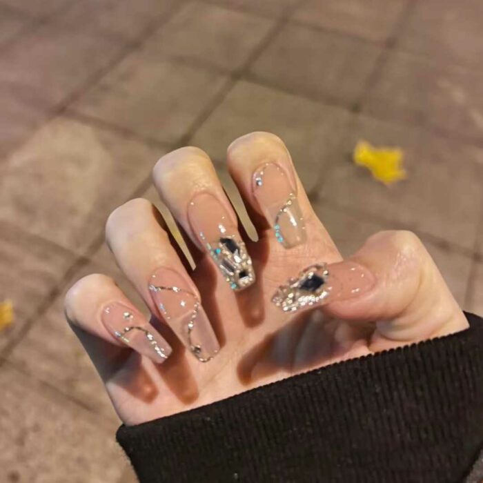 uñas de una mujer transparentes con decoraciones doradas 