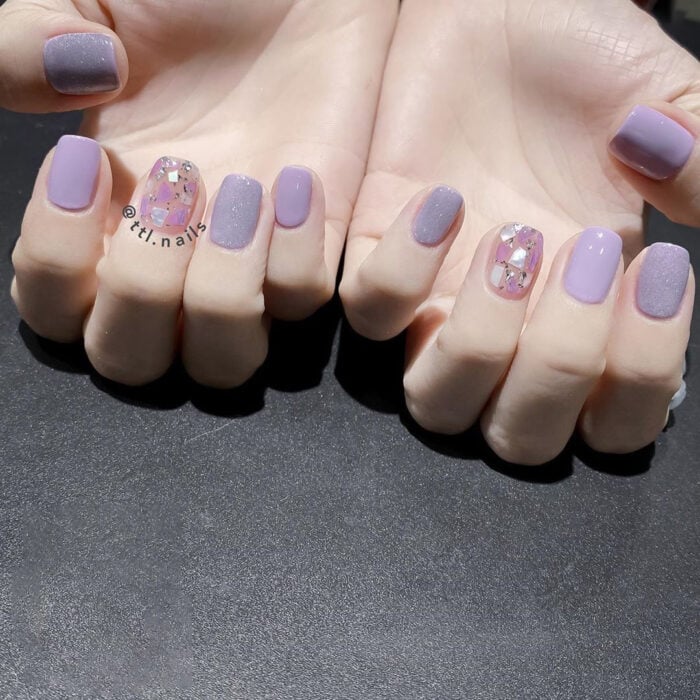 manos con la manicura en color lila con dos en colores glitter 