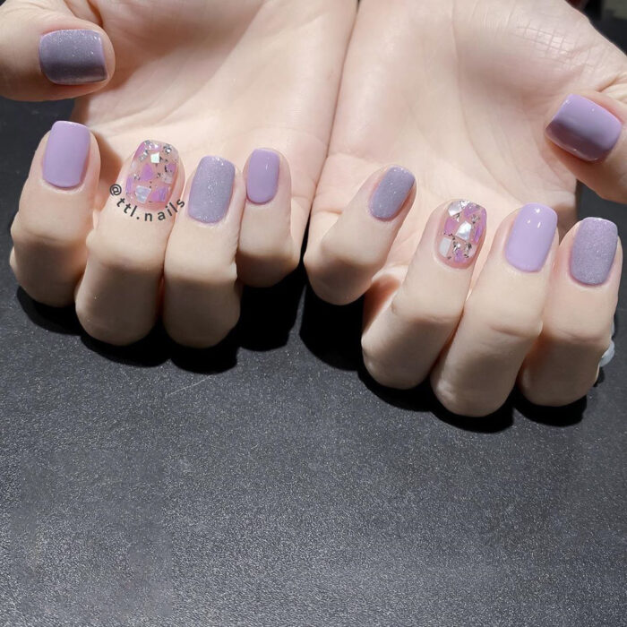 hands with manicure in lilac color with two in glitter colors 