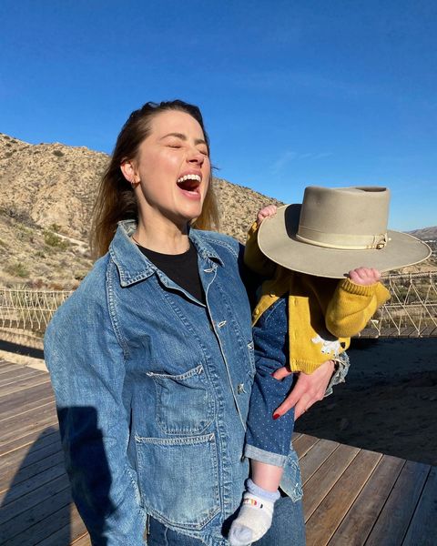 Amber Heard cargando a su hija que trae un sombrero en la cara 