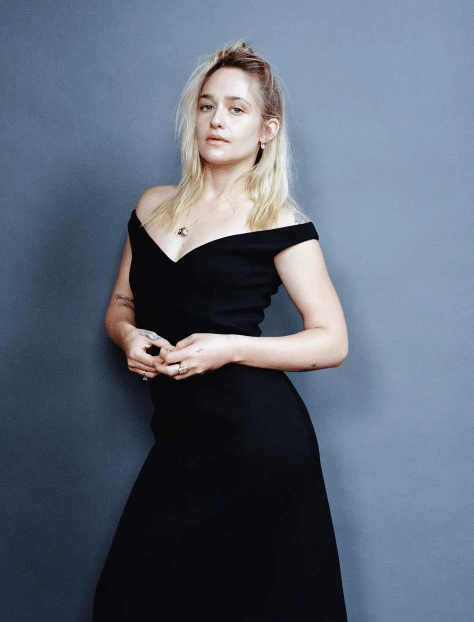 Jemima Kirke posando con un vestido negro en un fondo azul 