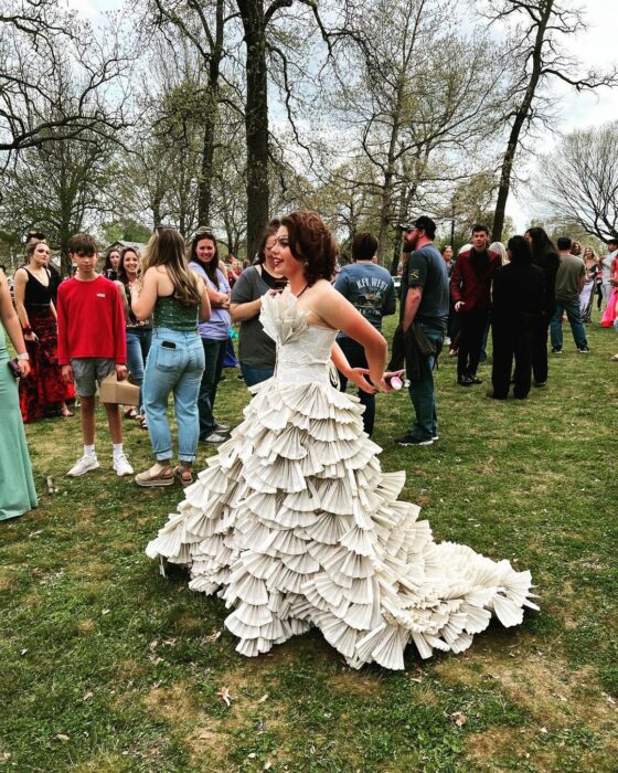 Young woman wearing dress with leaves of a book in the middle of a garden surrounded by people 