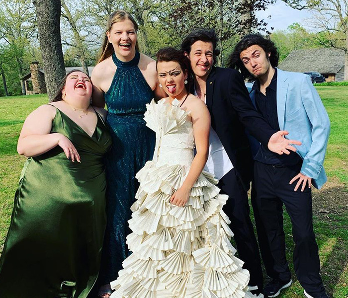 Chica posando con sus amigos portando un vestido con páginas de un libro 