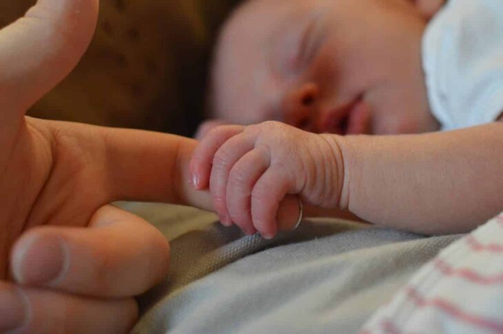 Sleeping newborn baby holding her mother's hand 