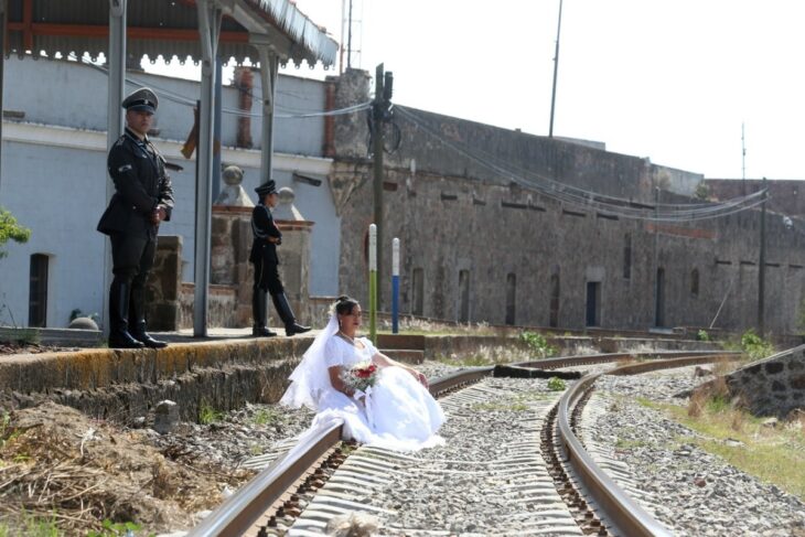 mujer vestida de novia sentada en las vías de un tren rodeada de hombres vestidos de soldados alemanes 