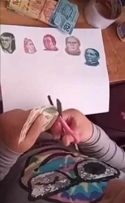 manos de una niña recortando billetes mexicanos para una tarea 