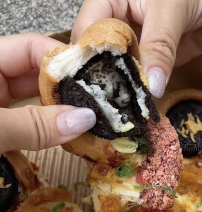 mano de una mujer partiendo una pizza con galleta Oreo rellena de queso 