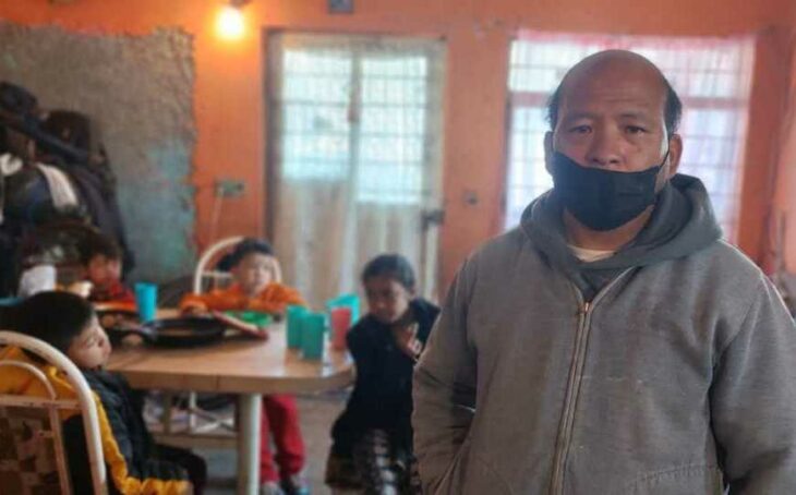 Fotografía de un hombre frente a un comedor donde están sus hijos