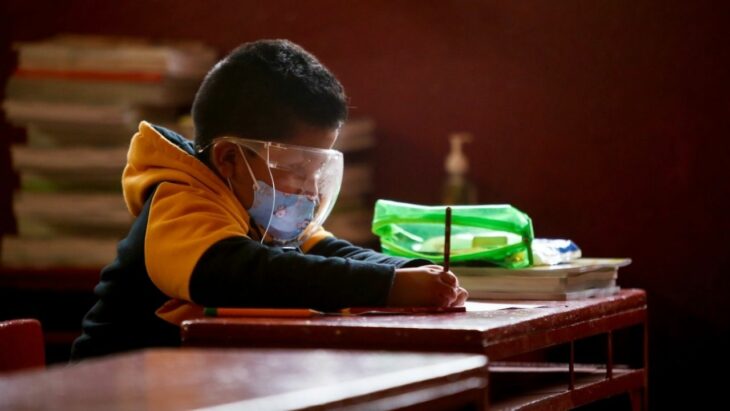 niño con careta sentado en la escuela escribiendo