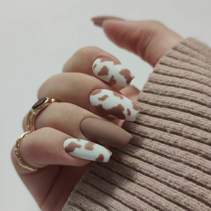 hand of a woman showing her acrylic nails in brown with a different design on one of the nails 