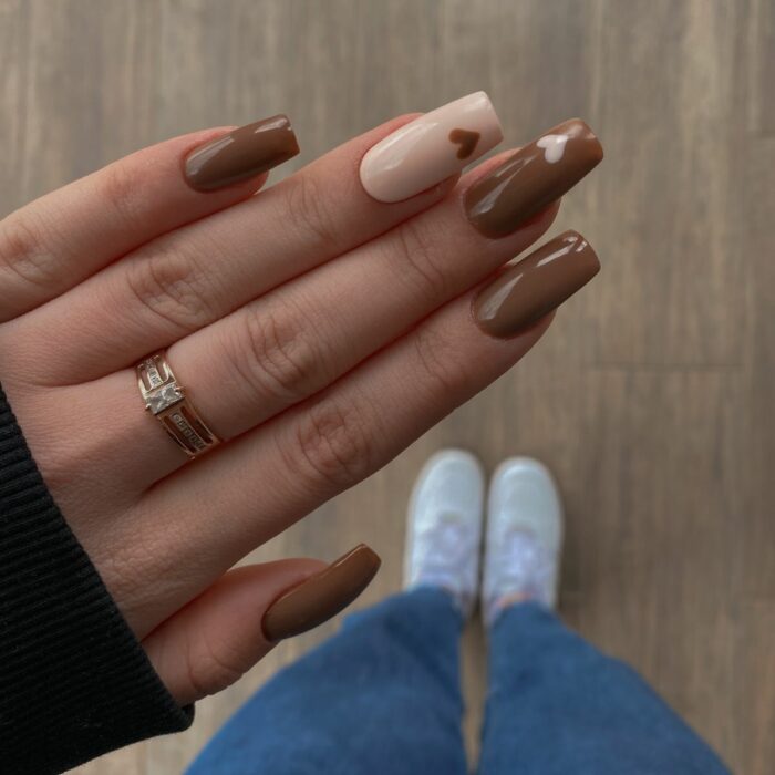 hands of a girl in brown with a nude nail and heart details 