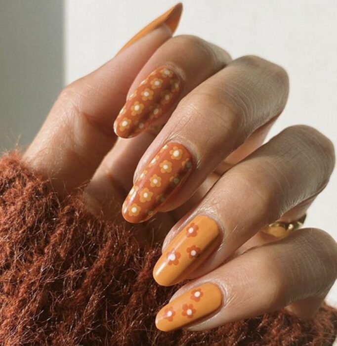 uñas de la mano de una chica en color naranja con flores del mismo color 