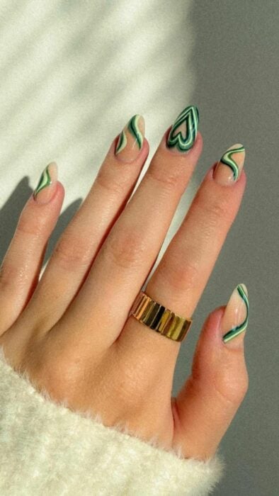 mano mostrando uñas acrílicas en color nude con ondas blancas y verdes 