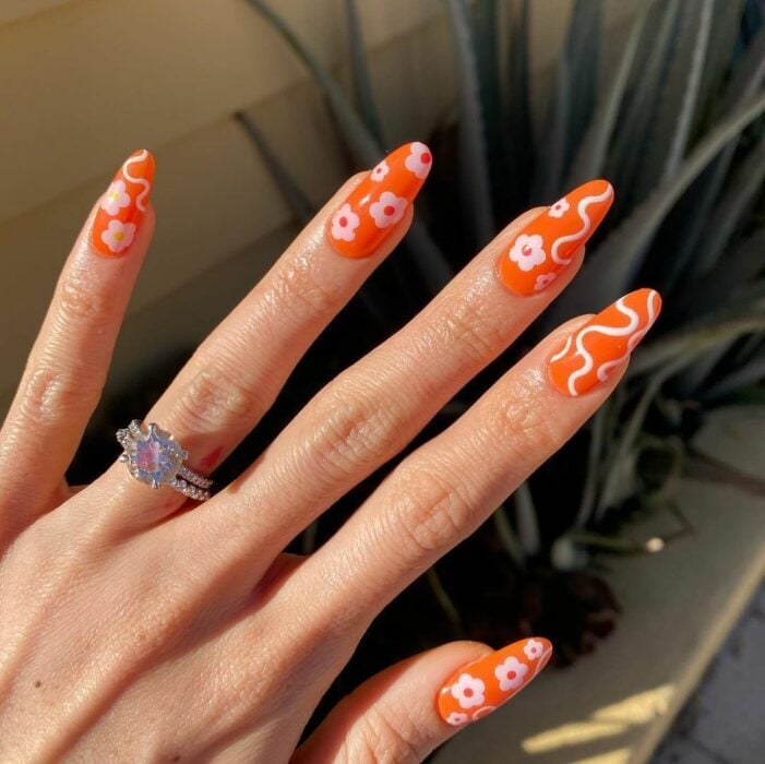 mano de una mujer mostrando las uñas acrílicas naranjas con detalles en color blanco