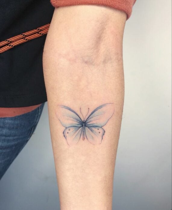 diseño de tatuaje de mariposa en color azul pastel en el antebrazo de una chica 