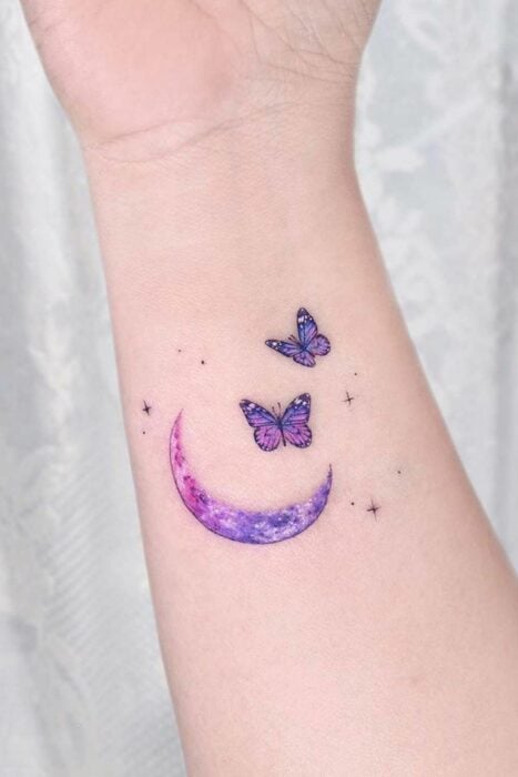 Tatuaje con el diseño de una luna debajo de dos mariposas en el antebrazo de una persona