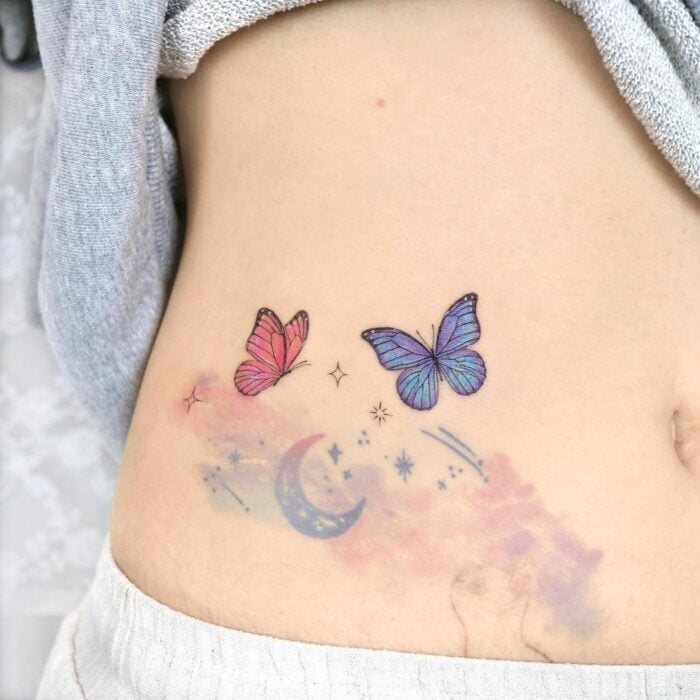 tatuaje en el estomago de una chica con el diseño de mariposas con luna y flores 