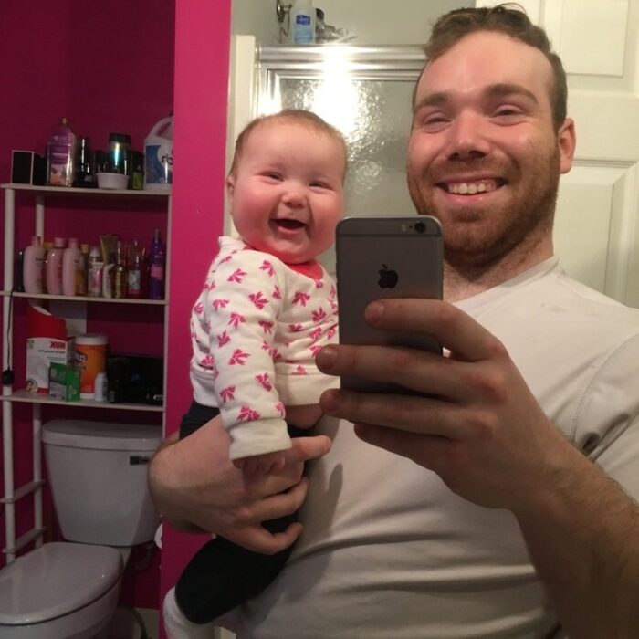 fotografía de un hombre sonriendo mientras carga a su hija frente al espejo del baño 