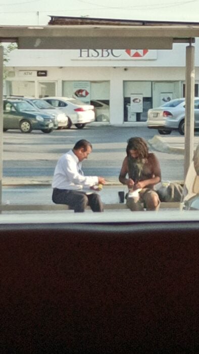 imagen de un hombre compartiendo su comida con un indigente en la parada de un autobús 