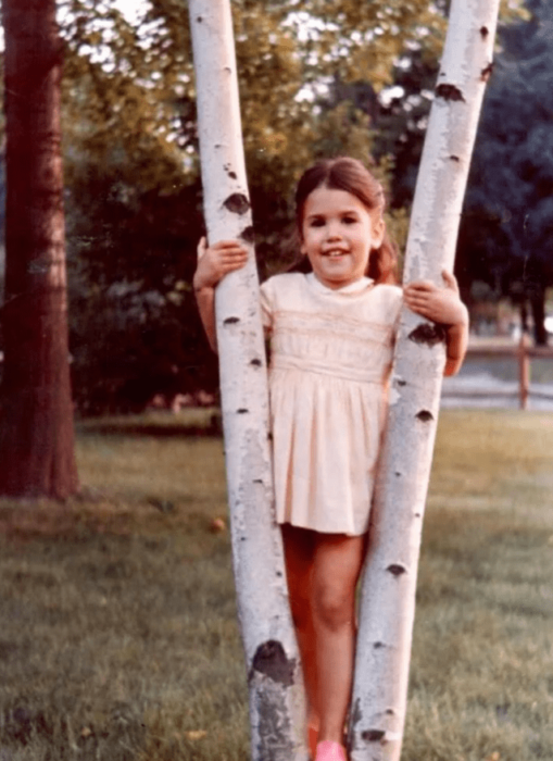 fotografía de una niña parada en medio de las ramas de un árbol 