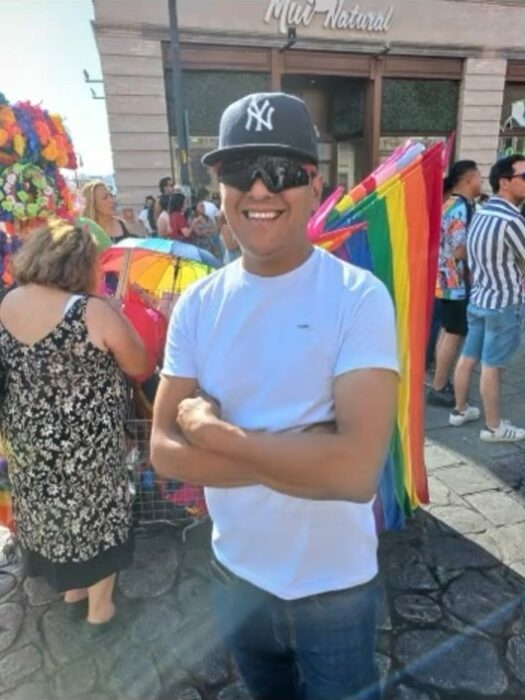 hombre con los brazos cruzados frente a una bandera del orgullo gay 