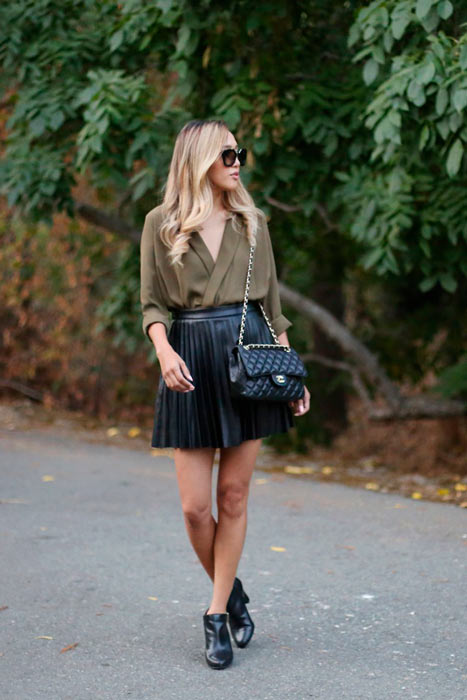 mujer posando a lado de unas ramas de árbol con falda negra y blusa color oliva y botines en color negro 