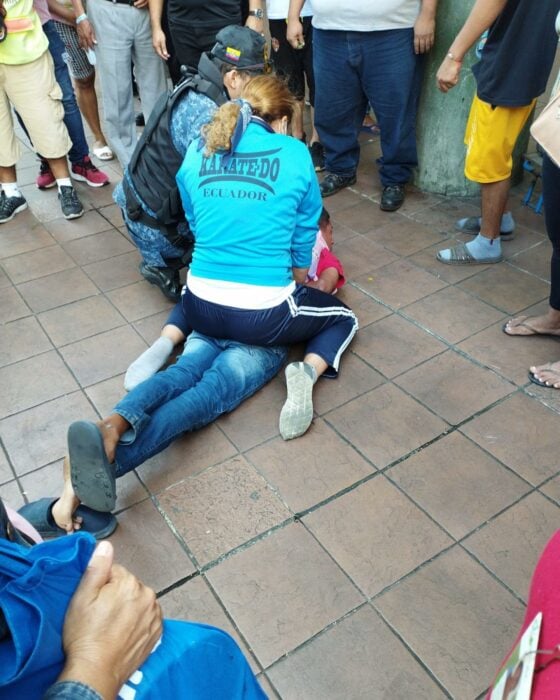 mujer sometiendo a un hombre en el suelo a lado de un oficial de policía en Ecuador 