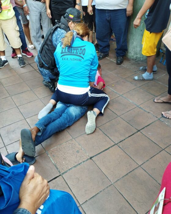 mujer sometiendo a un hombre en el suelo a lado de un oficial de policía en Ecuador 