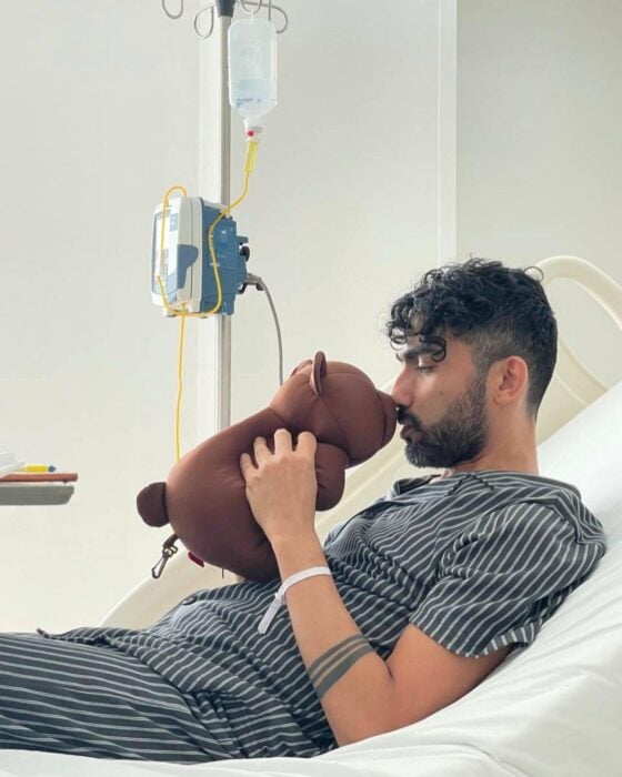 man in hospital bed putting his face in front of brown teddy bear 