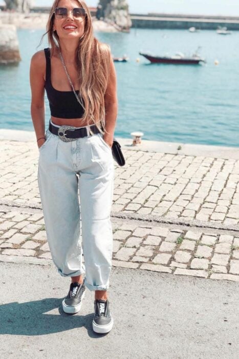 chica parada a la orilla de un malecón usando mom jeand combinado con un top negro y tenis casuales 