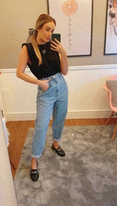 mujer tomándose una foto en el espejo luciendo un outfit con mom jeans y zapato de piso 