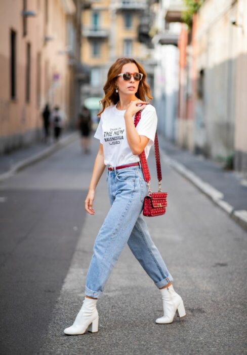 mujer cruzando una calle mientras posa sus mom jeans con botas en color blanco 